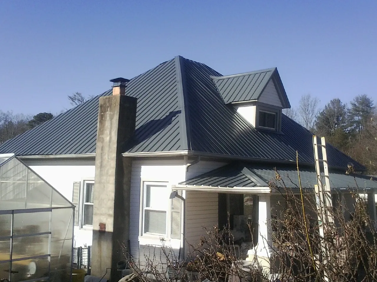 Dark blue standing seam metal roof on a white farmhouse with dormer — Slate & Tile Roof Repair by Roofing Brothers in Sale City
