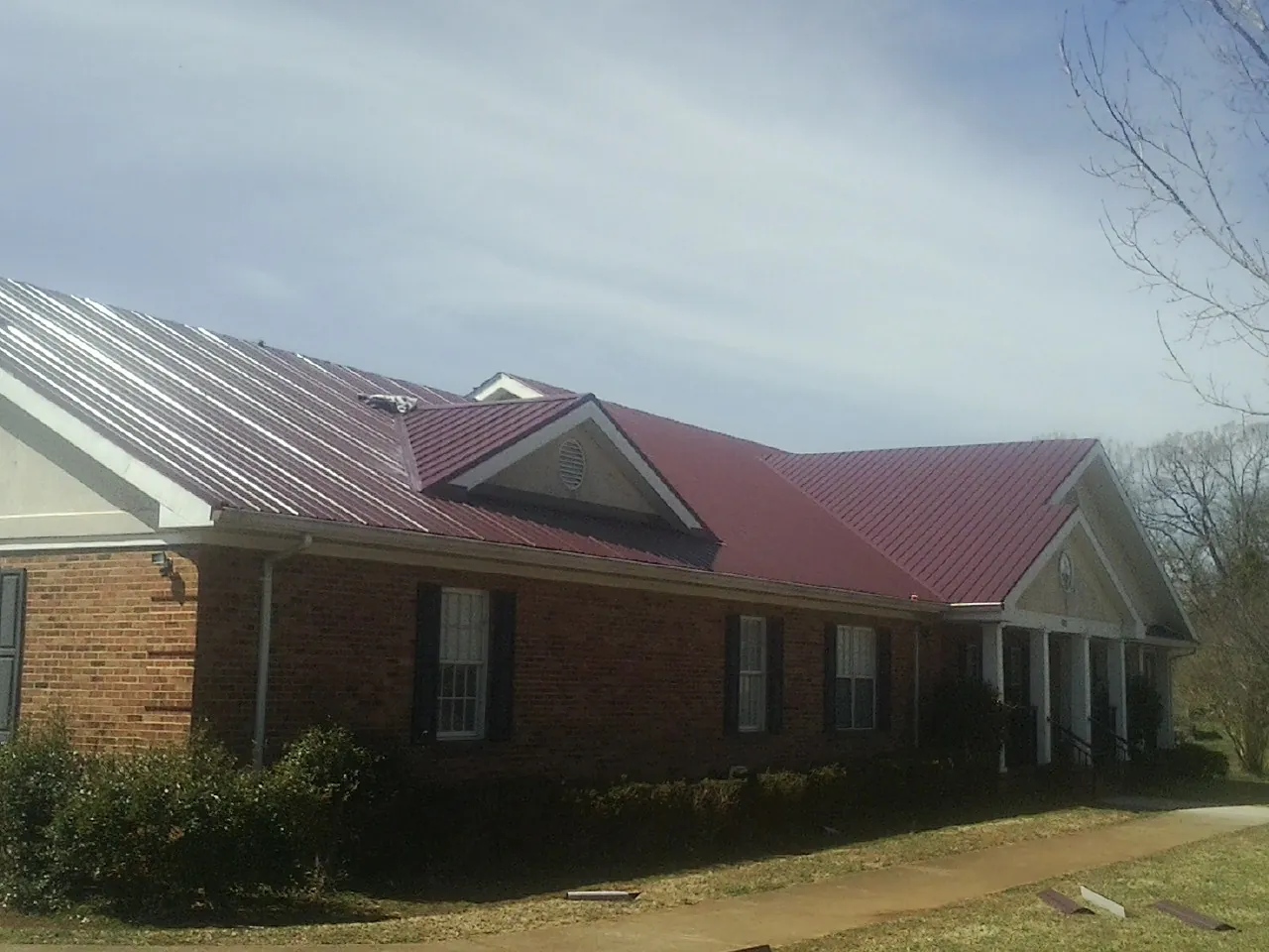 Red metal roof with gabled entries on a long brick building, from a Hail Damage Roof Repair job in Sale City