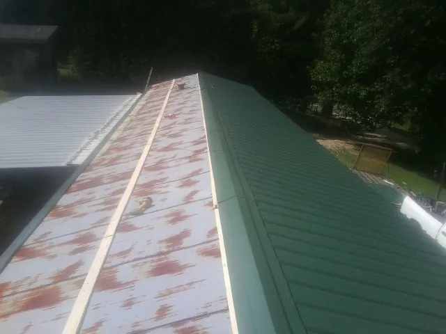 Old rusted panels beside newly installed green metal roofing — Wind Damage Roof Repair by Roofing Brothers in Sale City