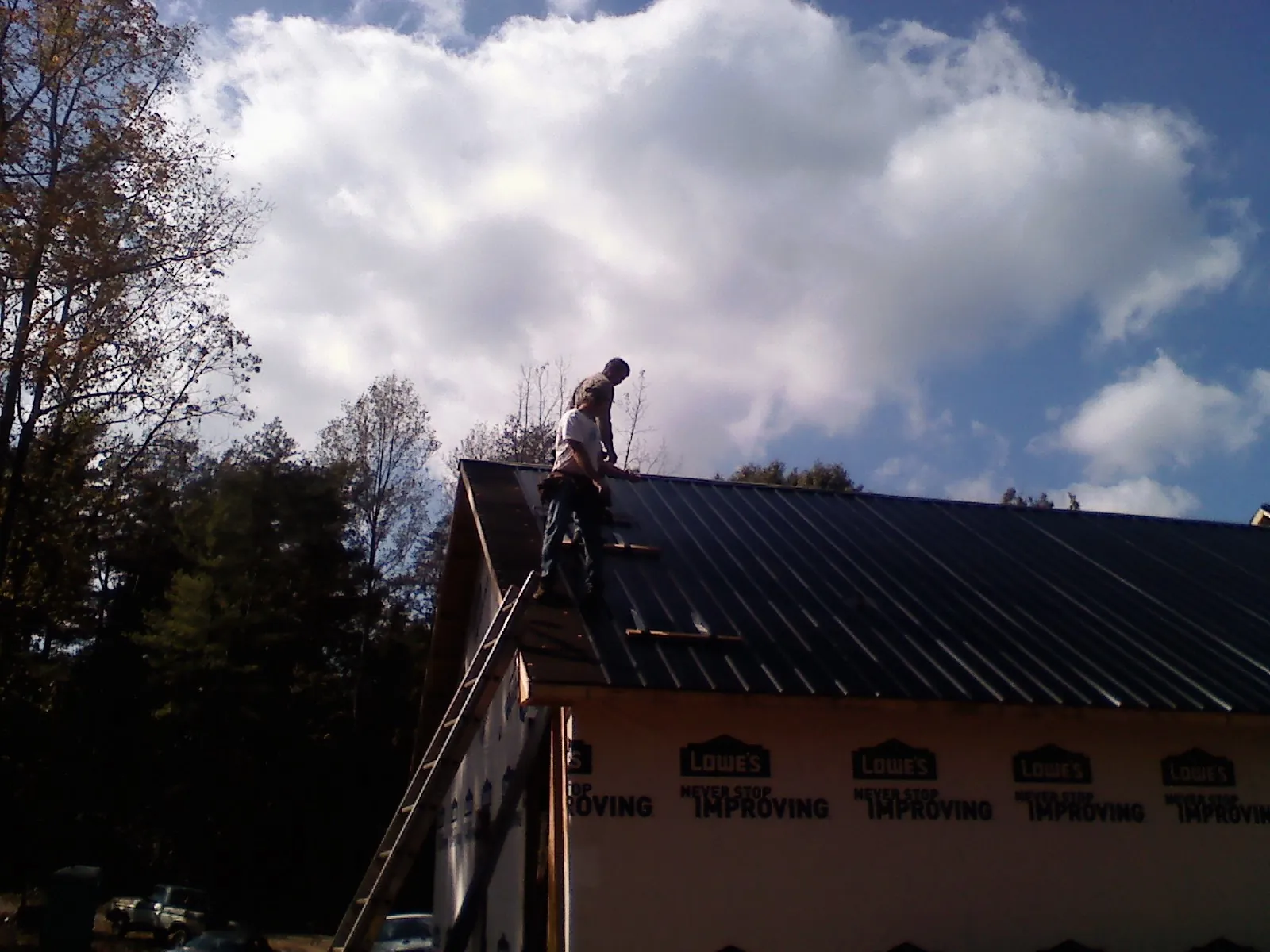 Roofer fastening dark metal panels high against a cloudy sky, from a Roof Inspection job in Sale City