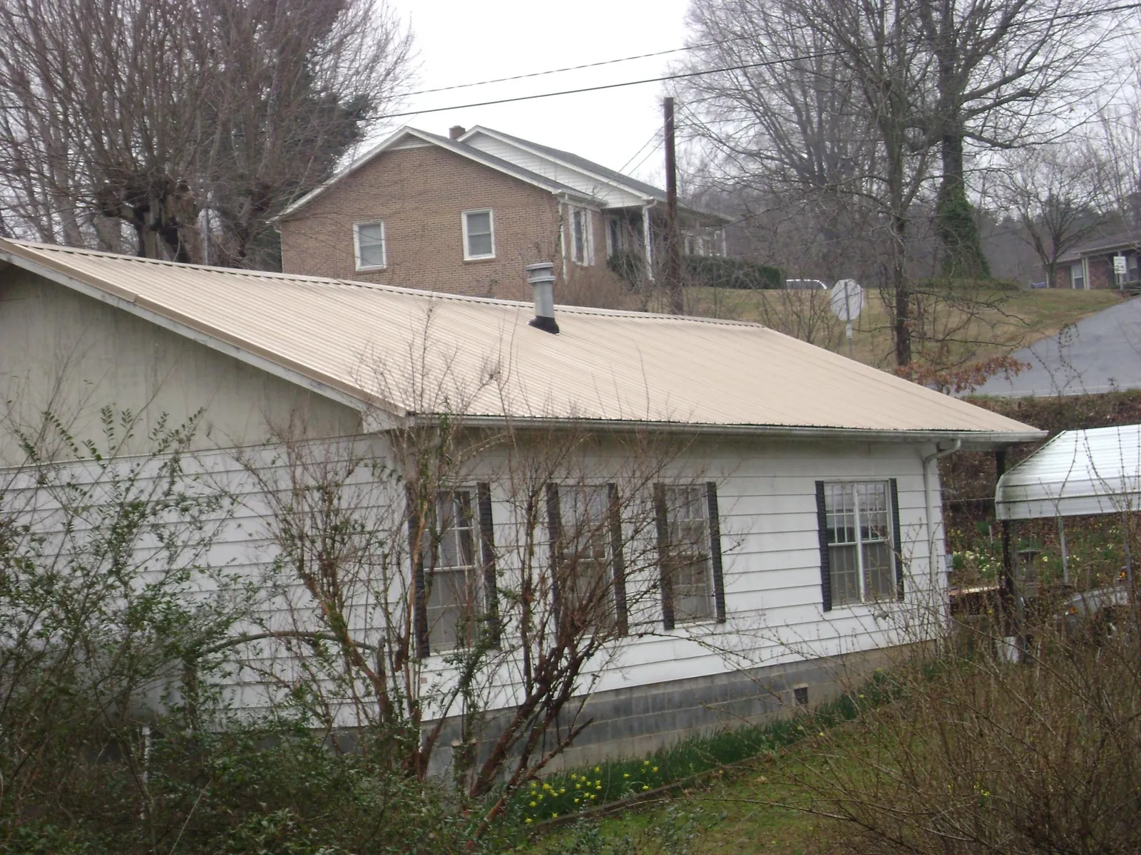 Tan metal roof on a white sided house set into a hillside — Commercial Roofing by Roofing Brothers in Sale City